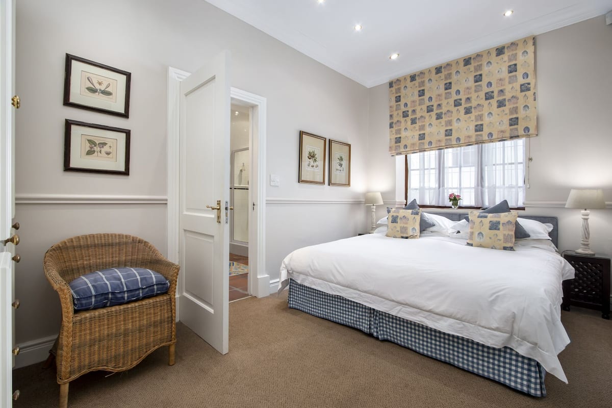 Un dormitorio con una cama grande, una silla de mimbre e impresiones botánicas enmarcadas en la pared.