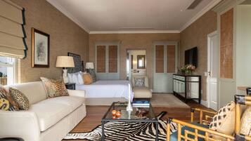 A spacious hotel room with a large bed, a sitting area with a sofa and armchairs, a coffee table, and a view of the hallway.