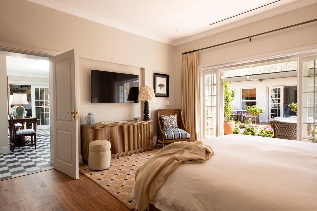 Un dormitorio con una cama grande, televisión, una silla y vista al jardín por la ventana.