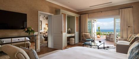 Amplia habitación de hotel con una cama grande, un área de estar con vistas al mar, televisión y balcón con mobiliario exterior.