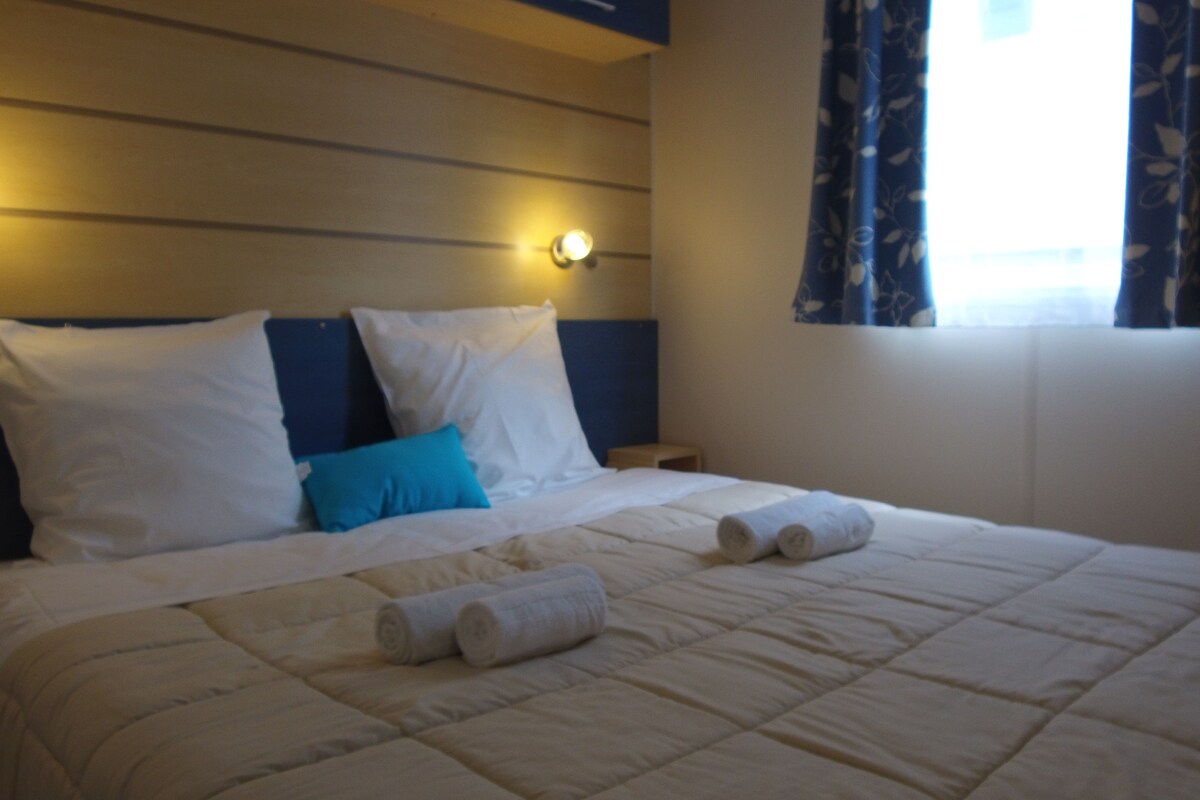 A hotel room with a bed, pillows, a nightstand, and a window with curtains.