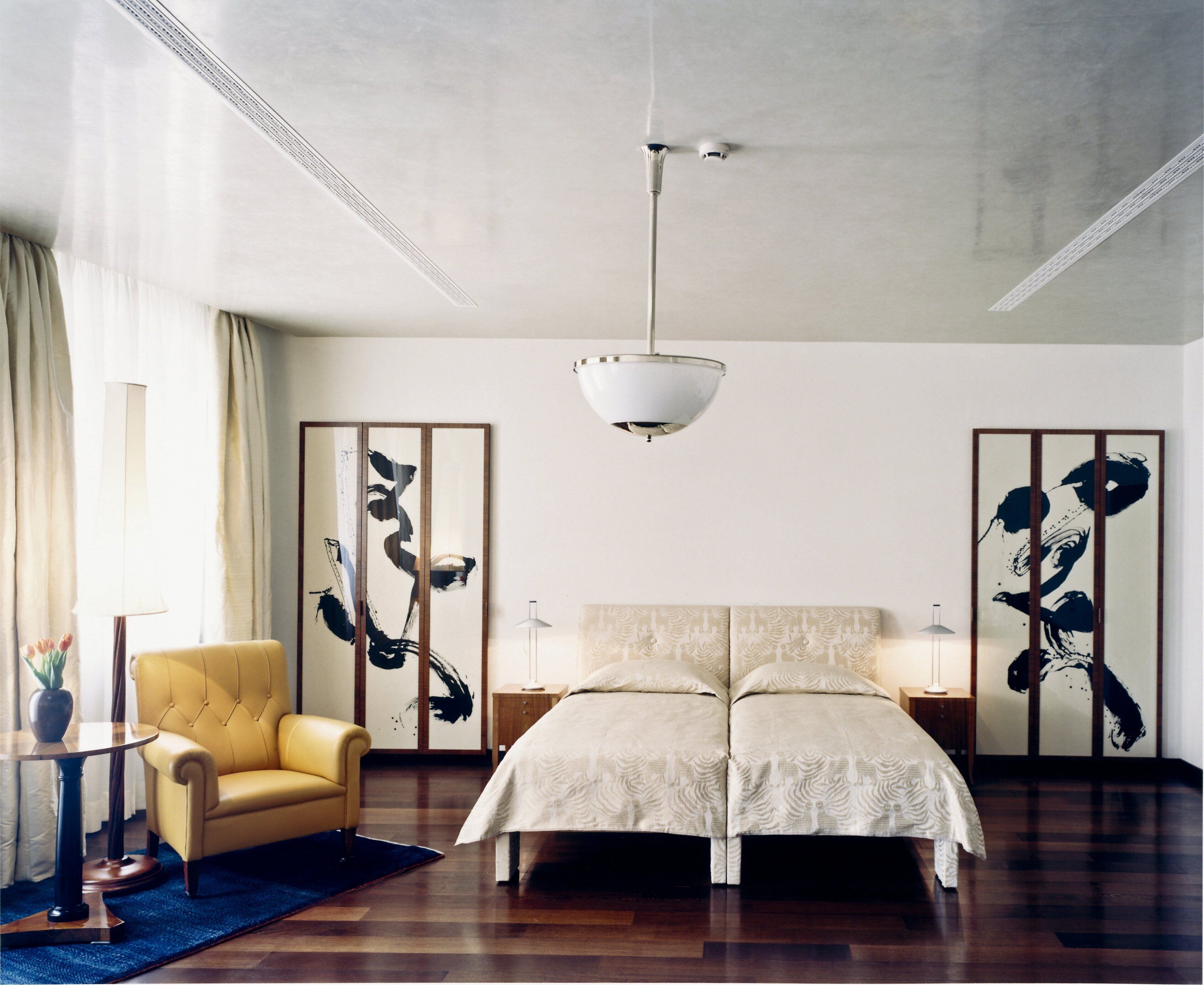 Ein Schlafzimmer mit einem Doppelbett, einem gelben Sessel, einer Stehlampe und einem Deckenventilator.