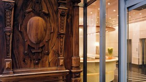 A wooden reception desk with intricate carvings, a glass entrance, and a modern interior.