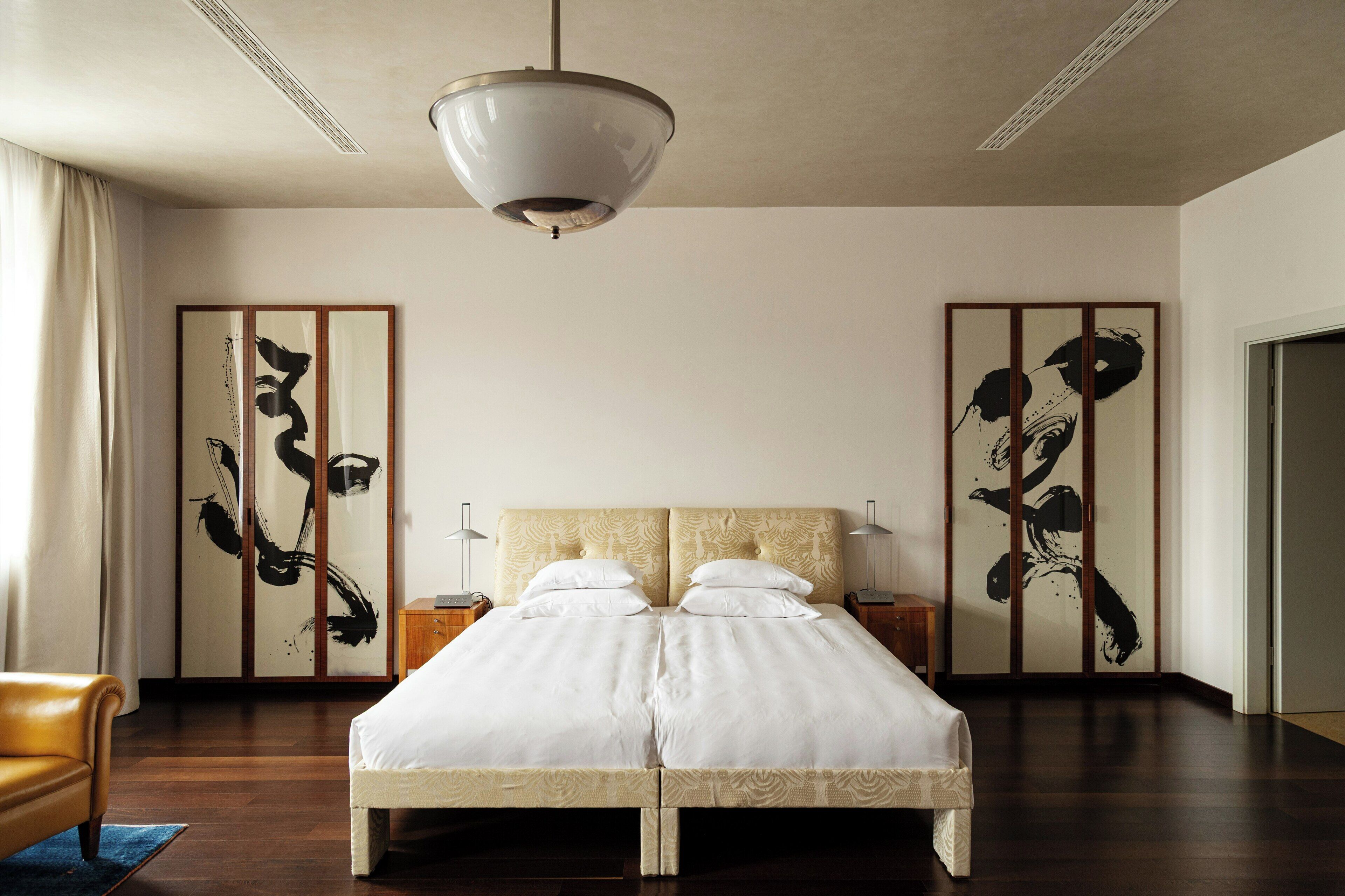 A hotel room with a large bed, a ceiling light, wooden floors, and traditional artwork on the walls.