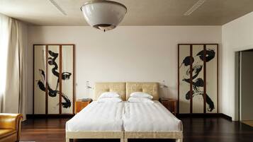 A hotel room with a large bed, a ceiling light, wooden floors, and traditional artwork on the walls.