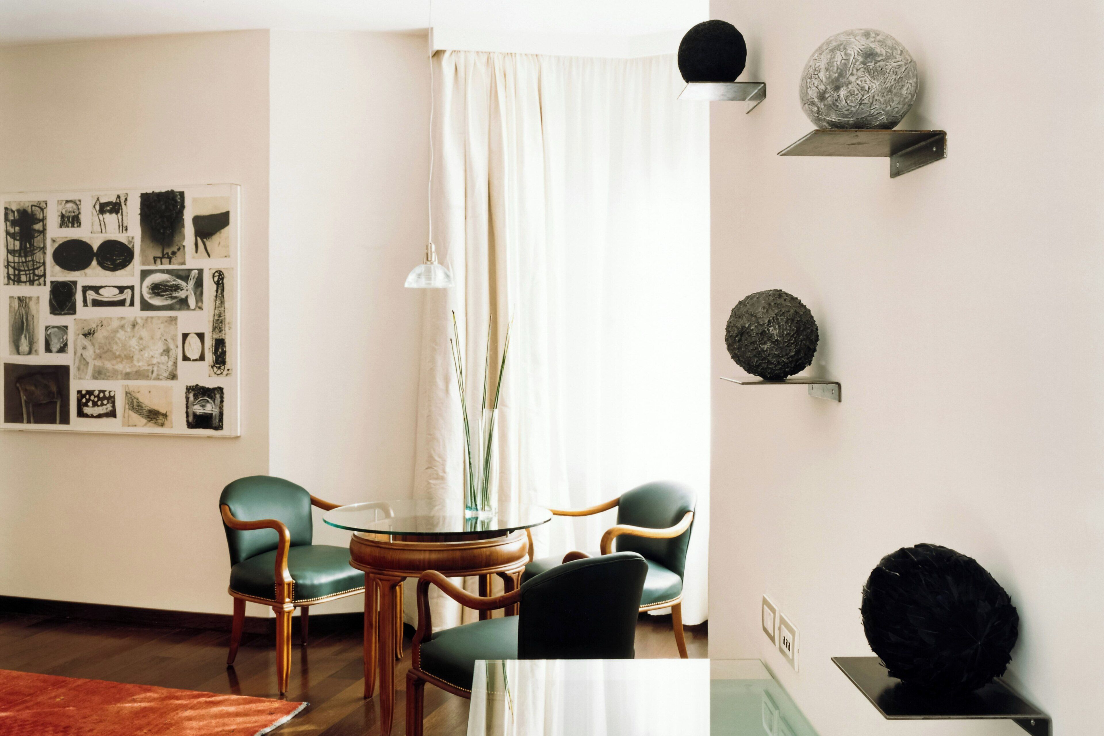 A dining area with a round table, two chairs, a vase, and wall art.