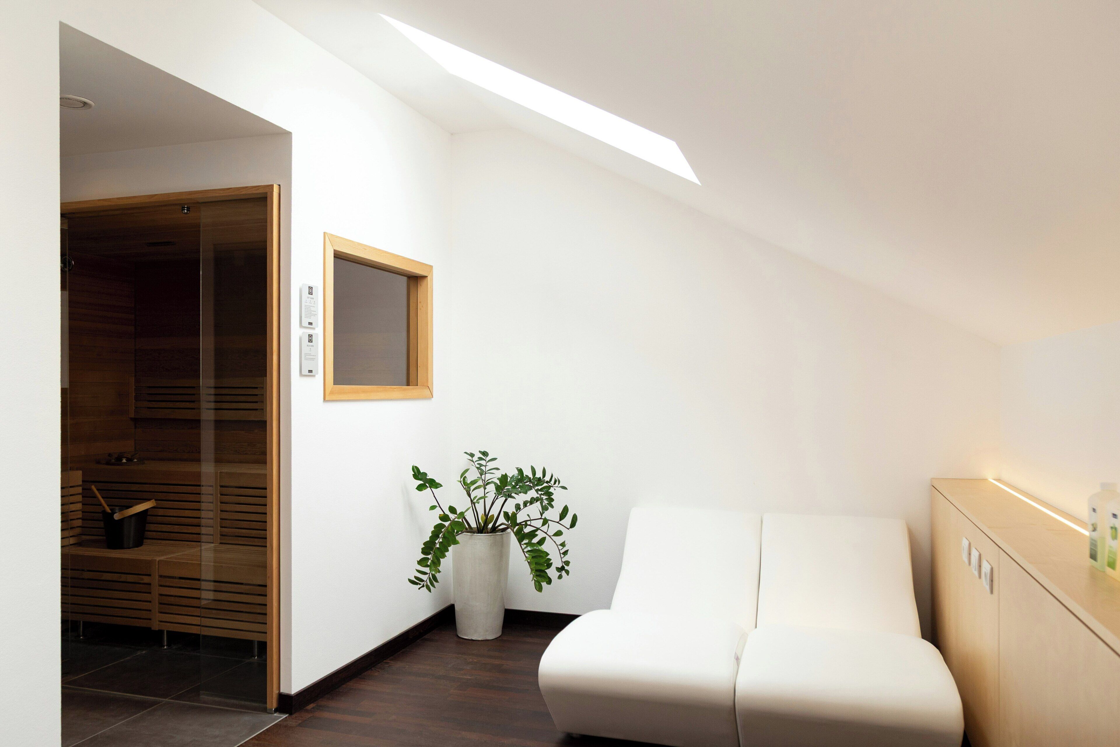 A modern room with a skylight, a white sofa, a wooden cabinet, and a potted plant.