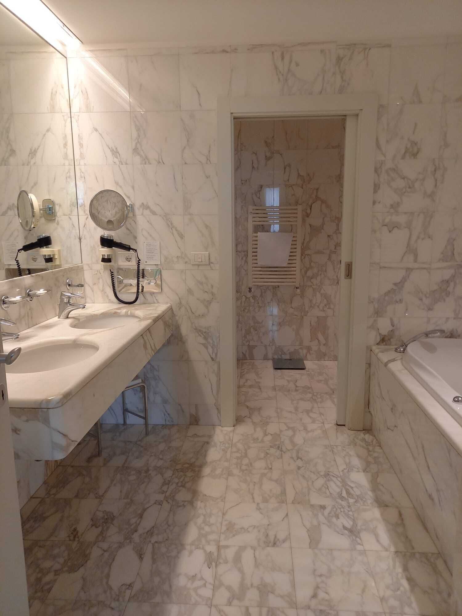 A bathroom with marble flooring, two sinks, a mirror, and a towel rack.