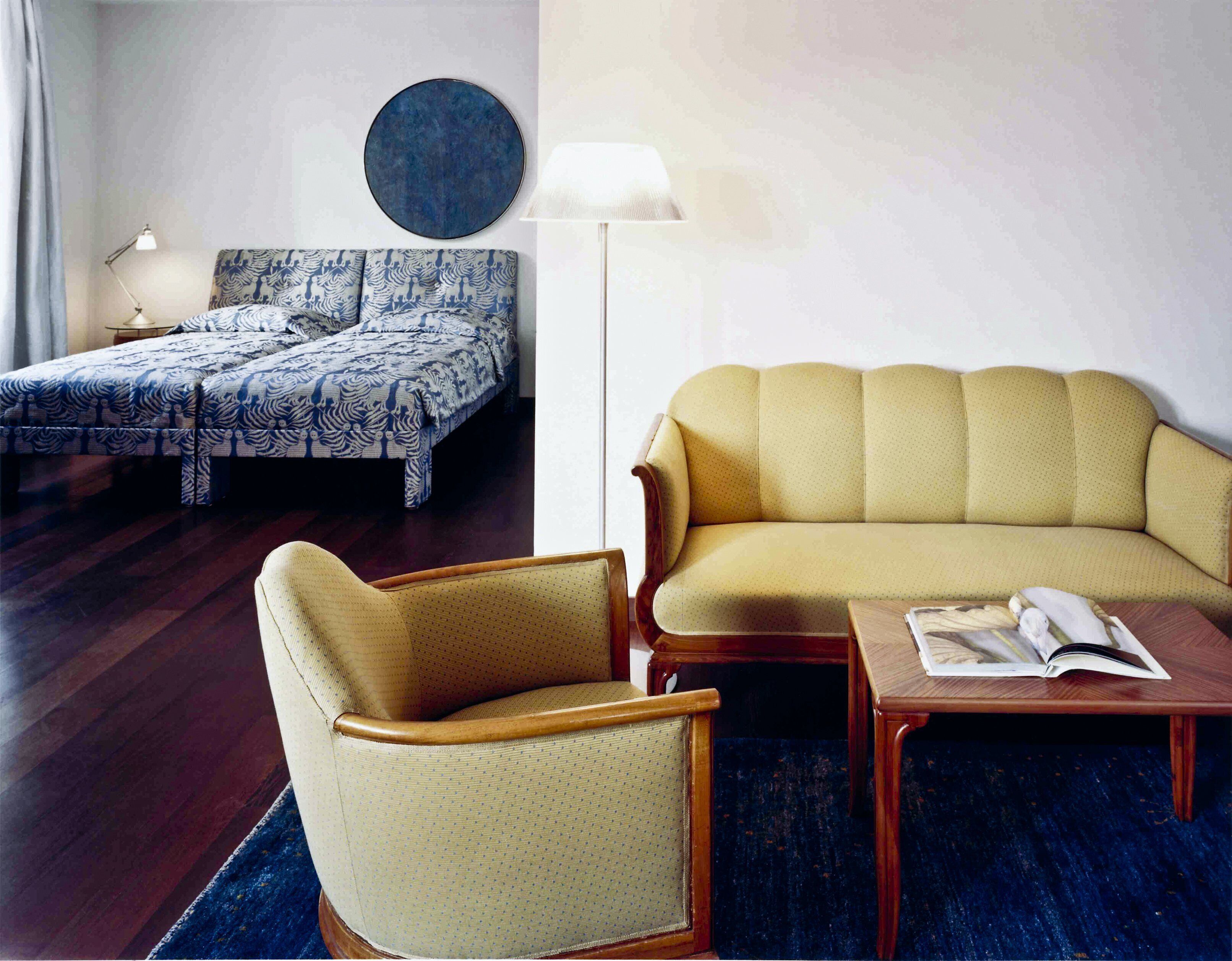 Um quarto com cama, sofá, poltrona, mesa e abajur.