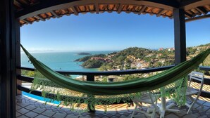A hammock on a balcony with a view of a coastal town and ocean.
