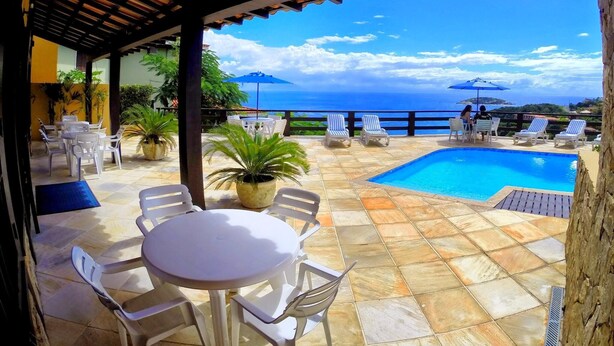 An outdoor seating area with a pool, chairs, and tables, overlooking a scenic ocean view.