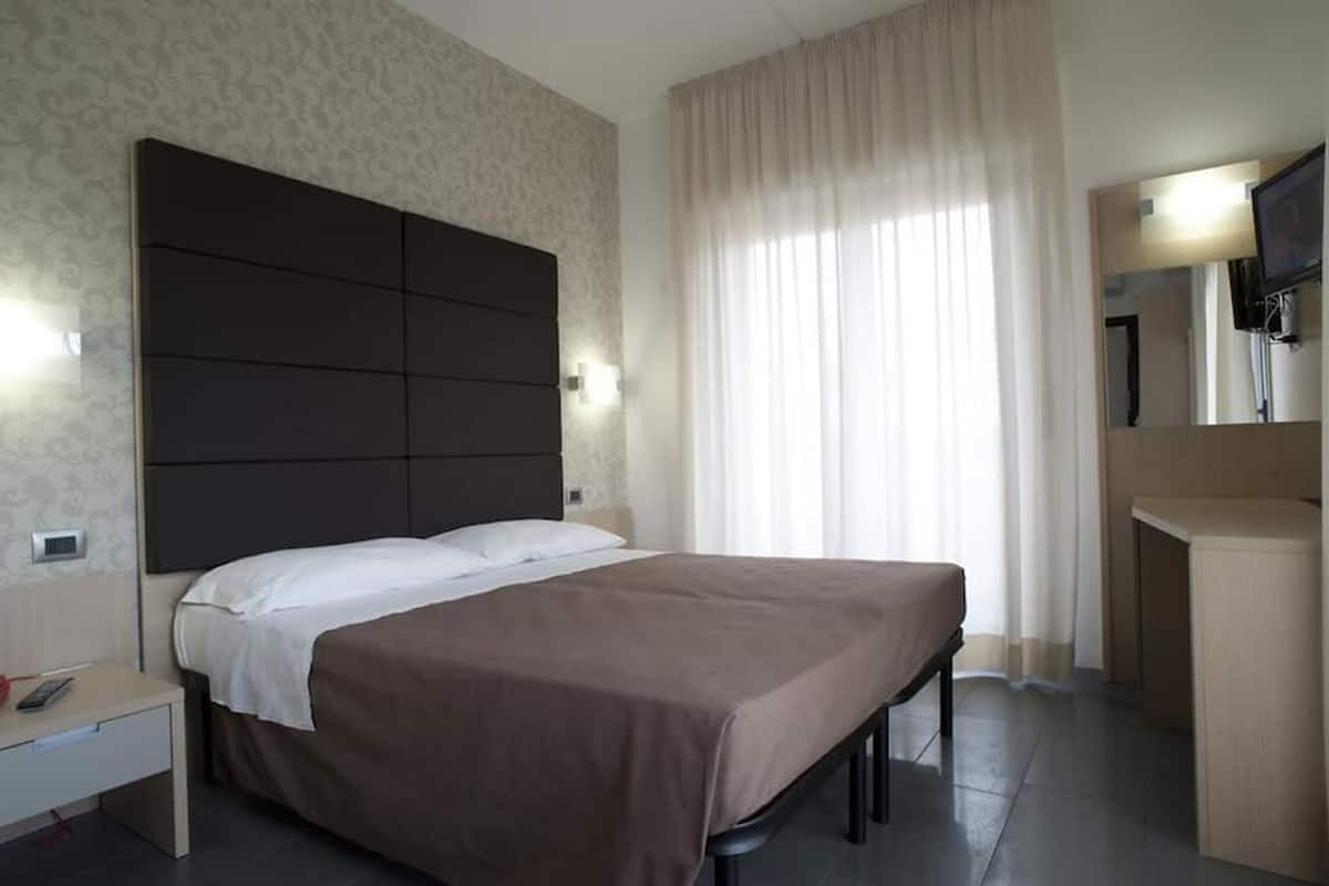 Una habitación de hotel con una cama grande, una mesita de noche, un espejo y un televisor.