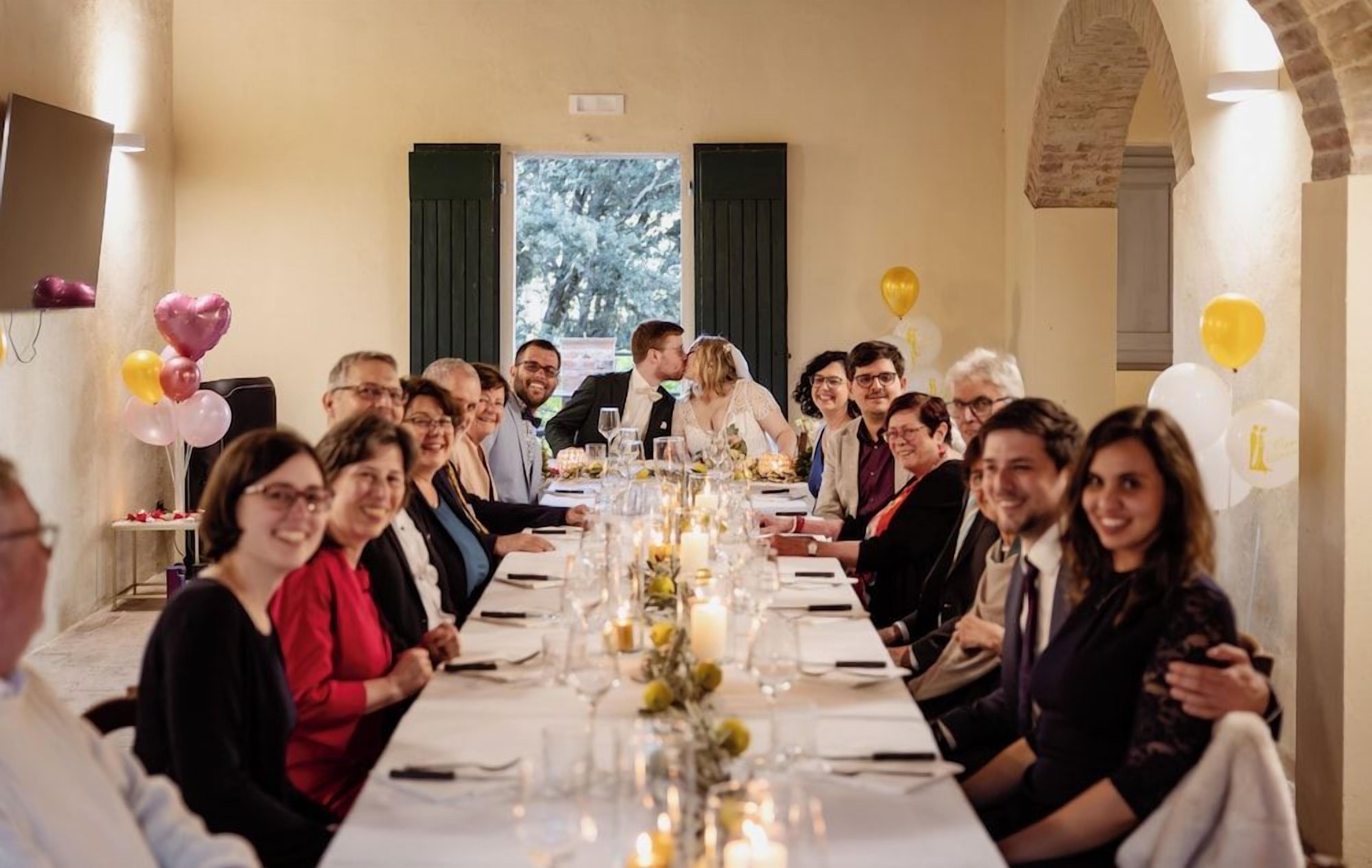 A long dining table with guests seated, a chandelier, and a view of the outdoors.