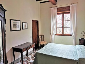 A room with a bed, a wooden desk, a chair, a window with curtains, and two framed pictures on the wall. - Fattoria il Bacio (Certaldo)