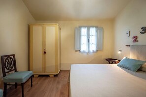 A bedroom with a bed, a wardrobe, a chair, a window, and a wall with numbers. - Fattoria il Bacio (Certaldo)