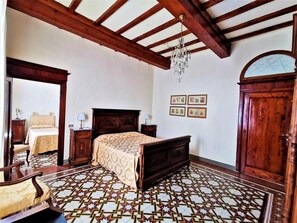 A bedroom with a large bed, wooden furniture, a chandelier, and patterned floor tiles.