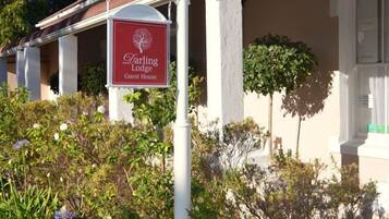 A white street lamp with a sign for Darling Lodge Guest House in front of a building with a brown roof and white trim.