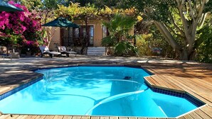 A swimming pool with a wooden deck, lounge chairs, and a covered seating area.
