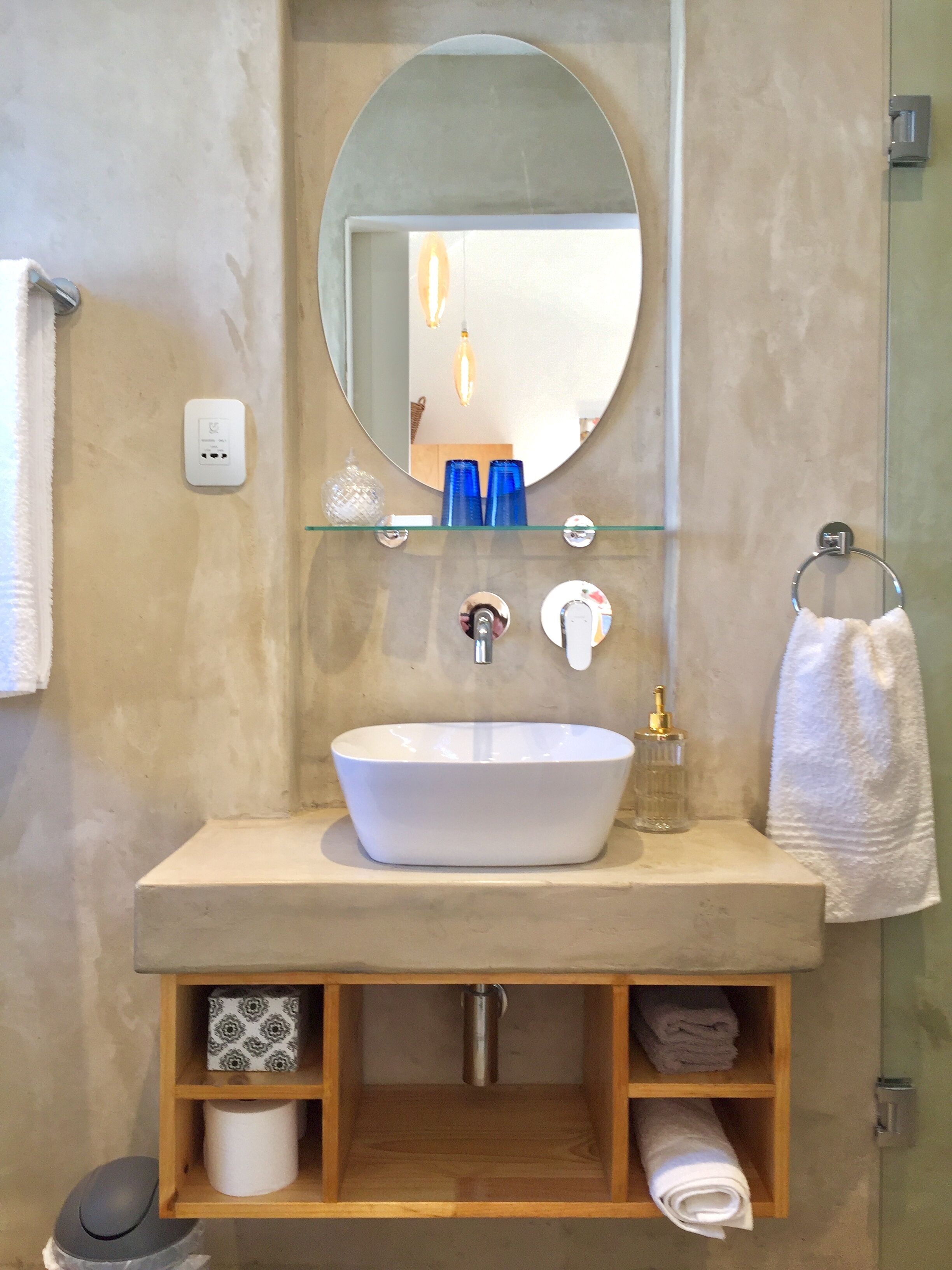 A bathroom with a white sink, a mirror, a towel rack, and a shelf with toiletries.