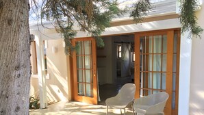 A covered patio with two wicker chairs, a wooden door, and a view into the house.