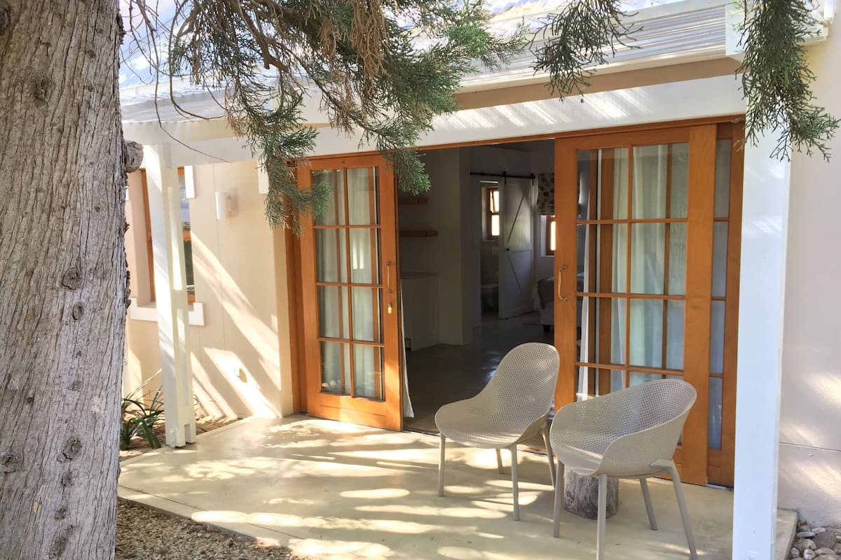 A covered patio with two wicker chairs, a wooden door, and a view into the house.