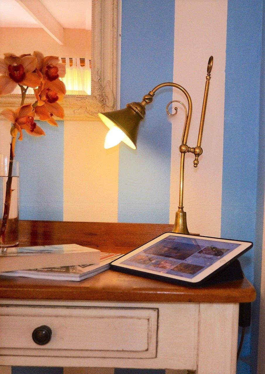Un escritorio con una tableta, una lámpara de escritorio de latón y un florero con flores.