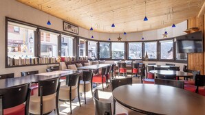 A restaurant with round tables and chairs, large windows, and a wooden ceiling. - VVF Val-Cenis Haute-Maurienne (Val-Cenis)
