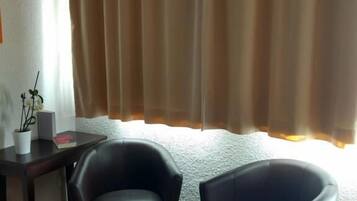 A room with two black leather chairs, a wooden table with a potted plant and a book, and a window with beige curtains.