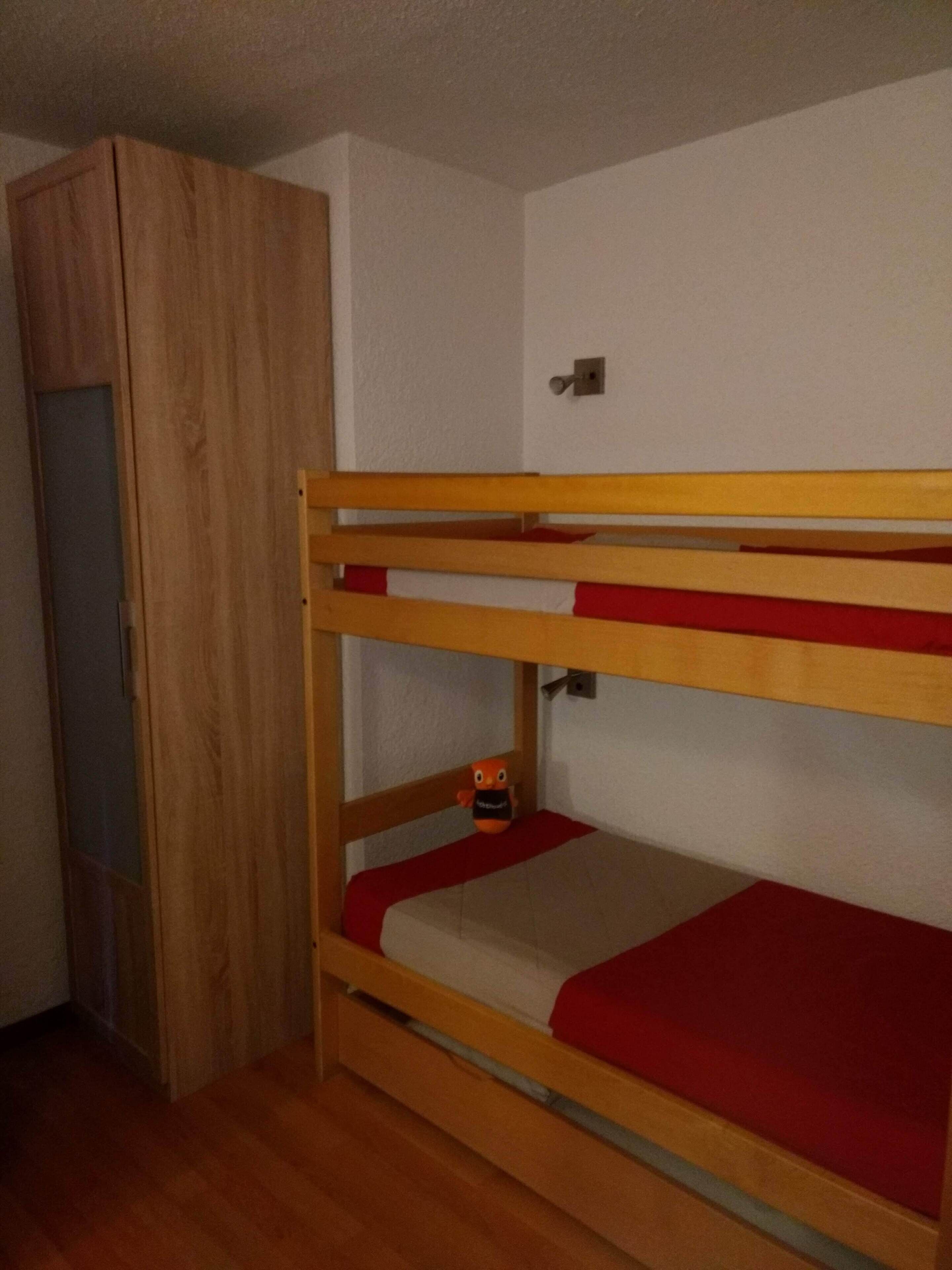 A bunk bed with a wooden frame and red bedding, a wardrobe, and a door.