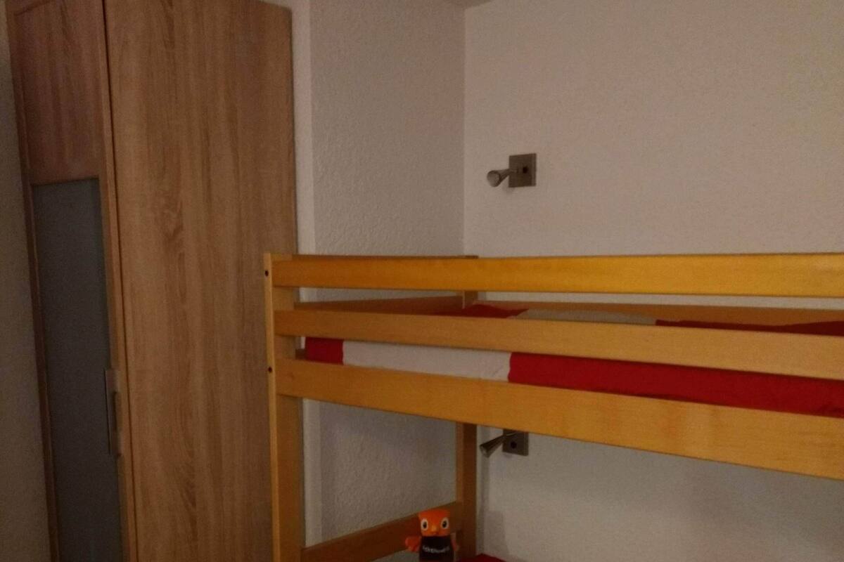 A bunk bed with a wooden frame and red bedding, a wardrobe, and a door.