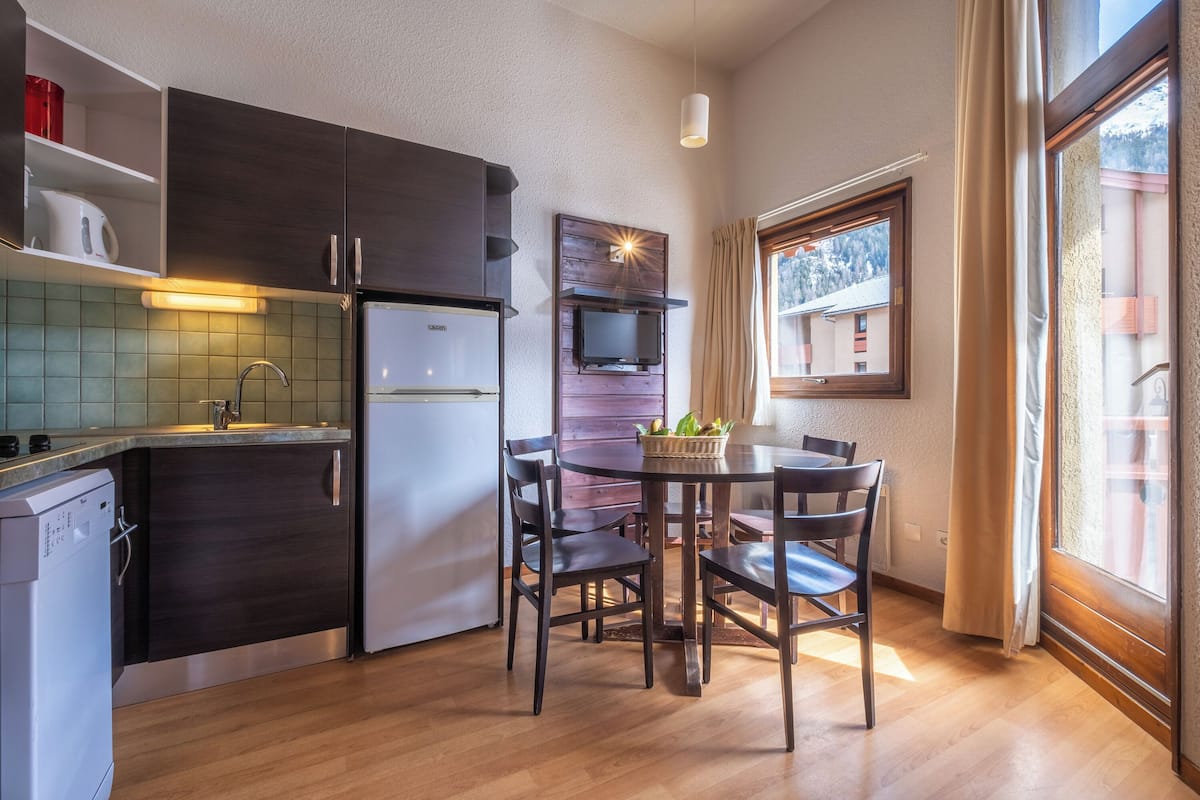A compact kitchen with dark cabinets, a white refrigerator, a microwave, and a small dining area with a table and chairs.