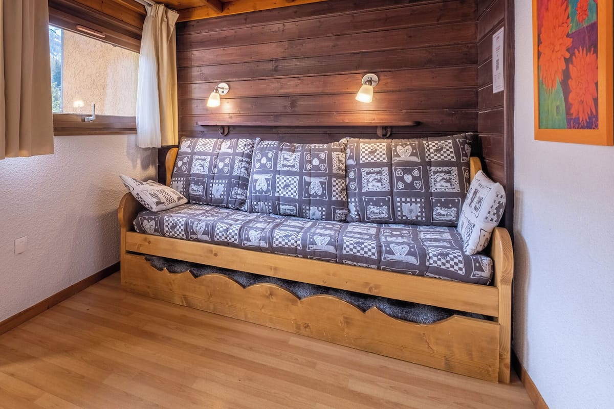 A wooden cabin interior with a built-in sofa, two wall-mounted lamps, and a window with curtains.