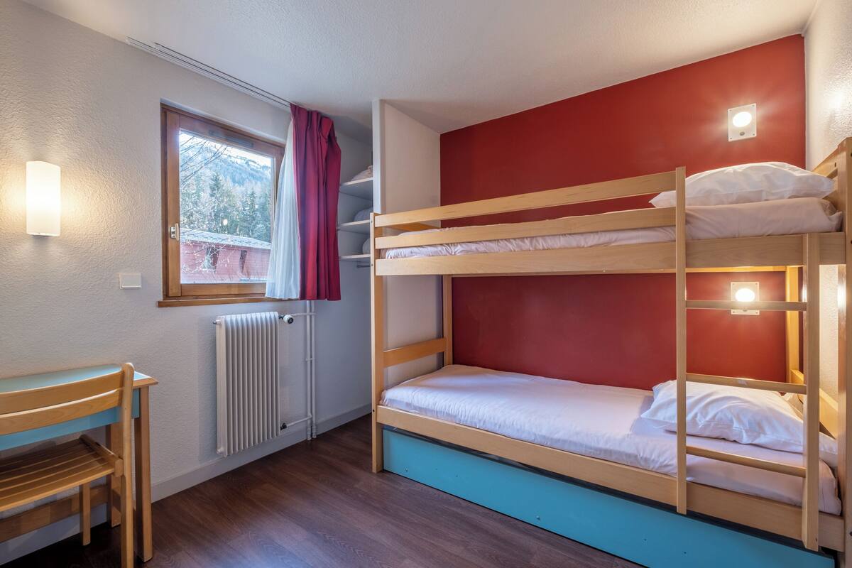 A bunk bed room with a window, a radiator, and a wooden desk.