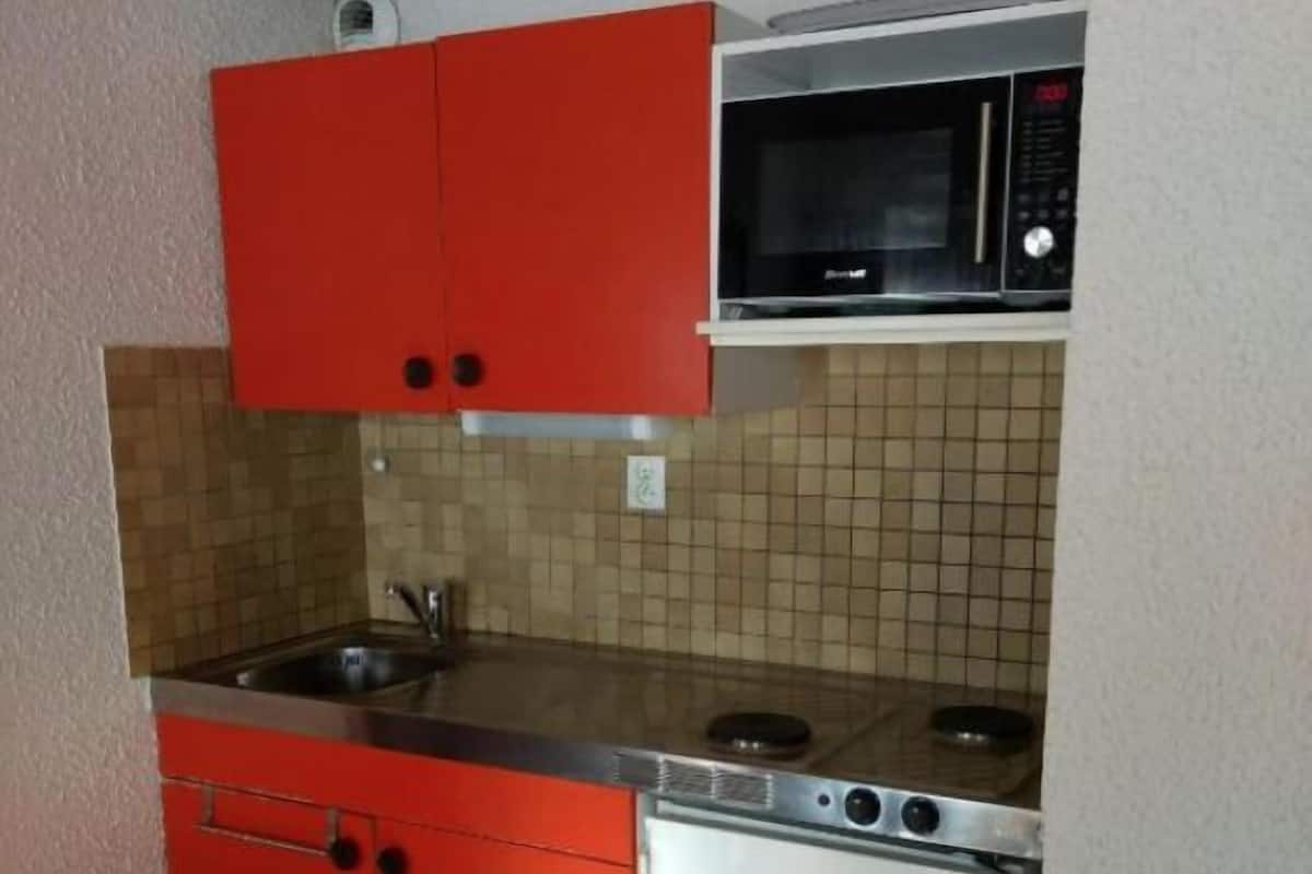 A compact kitchen with red cabinets, a microwave, a sink, and a dishwasher.