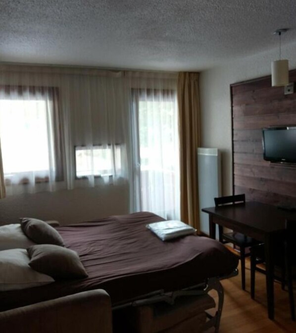 A hotel room with a bed, a desk, a chair, and a television on the wall.