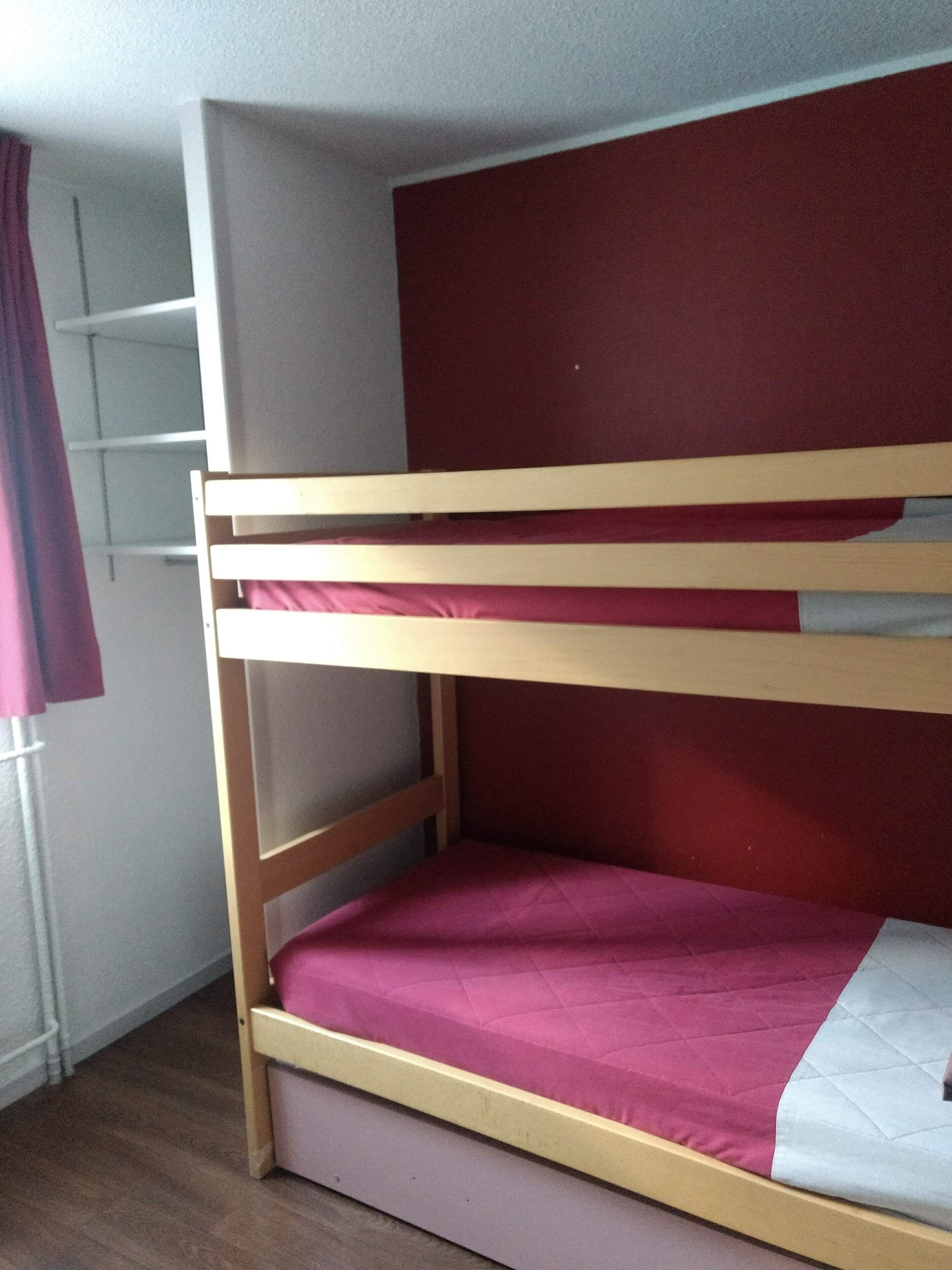 A bunk bed with two levels, a wooden frame, and a red and white mattress.