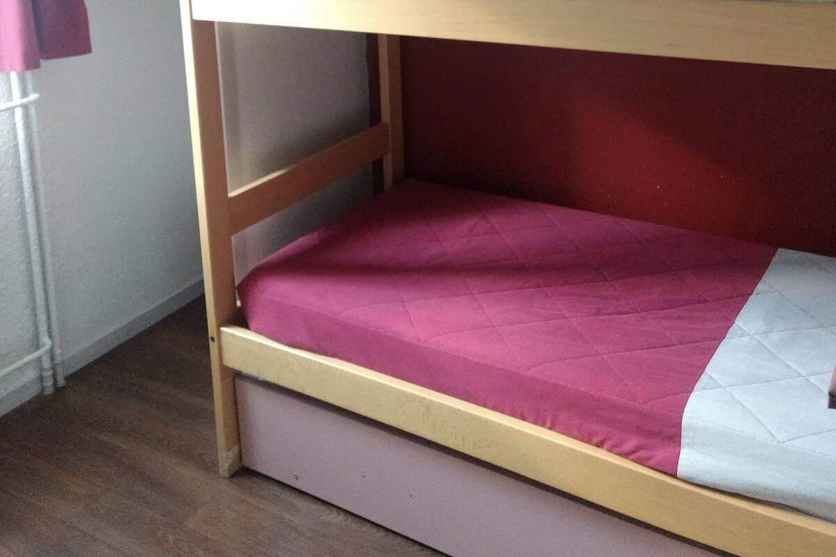 A bunk bed with two levels, a wooden frame, and a red and white mattress.