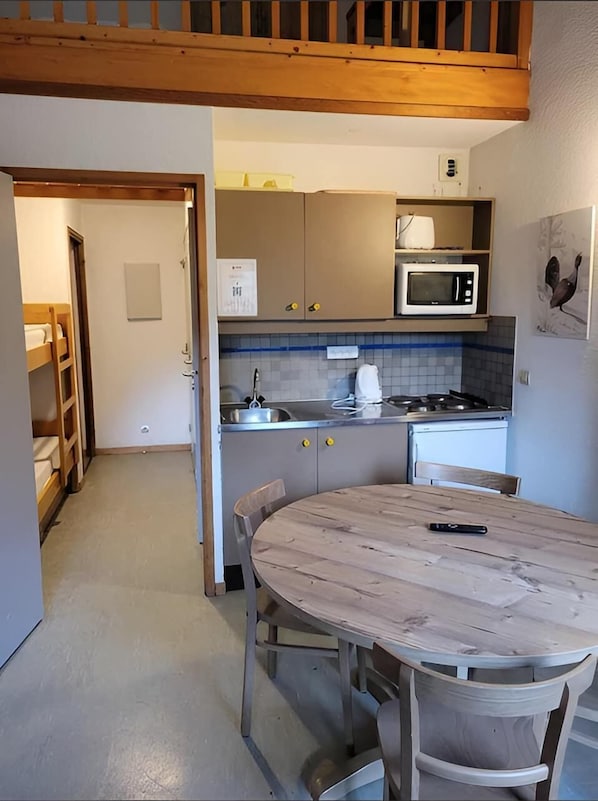 A compact kitchen with a microwave, stove, and sink. There is a wooden table with chairs and a bunk bed in the adjacent room. - VVF Val-Cenis Haute-Maurienne (Val-Cenis)