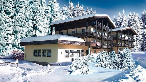 A two-story chalet with a balcony, surrounded by snow-covered trees. - Landhotel Traudl (Saalbach-Hinterglemm)