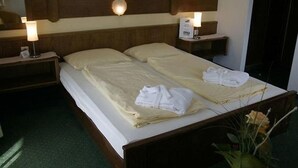 A double bed with white linens and towels, two bedside lamps, and a nightstand with a clock. - Landhotel Traudl (Saalbach-Hinterglemm)