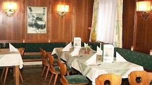 A restaurant with wooden paneled walls, green cushioned booths, and tables set with white tablecloths and napkins. - Landhotel Traudl (Saalbach-Hinterglemm)
