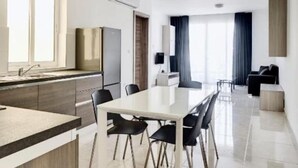 A modern kitchen with a dining area, a large window, and a flat-screen TV. - The Village Apartments (St. Paul's Bay)