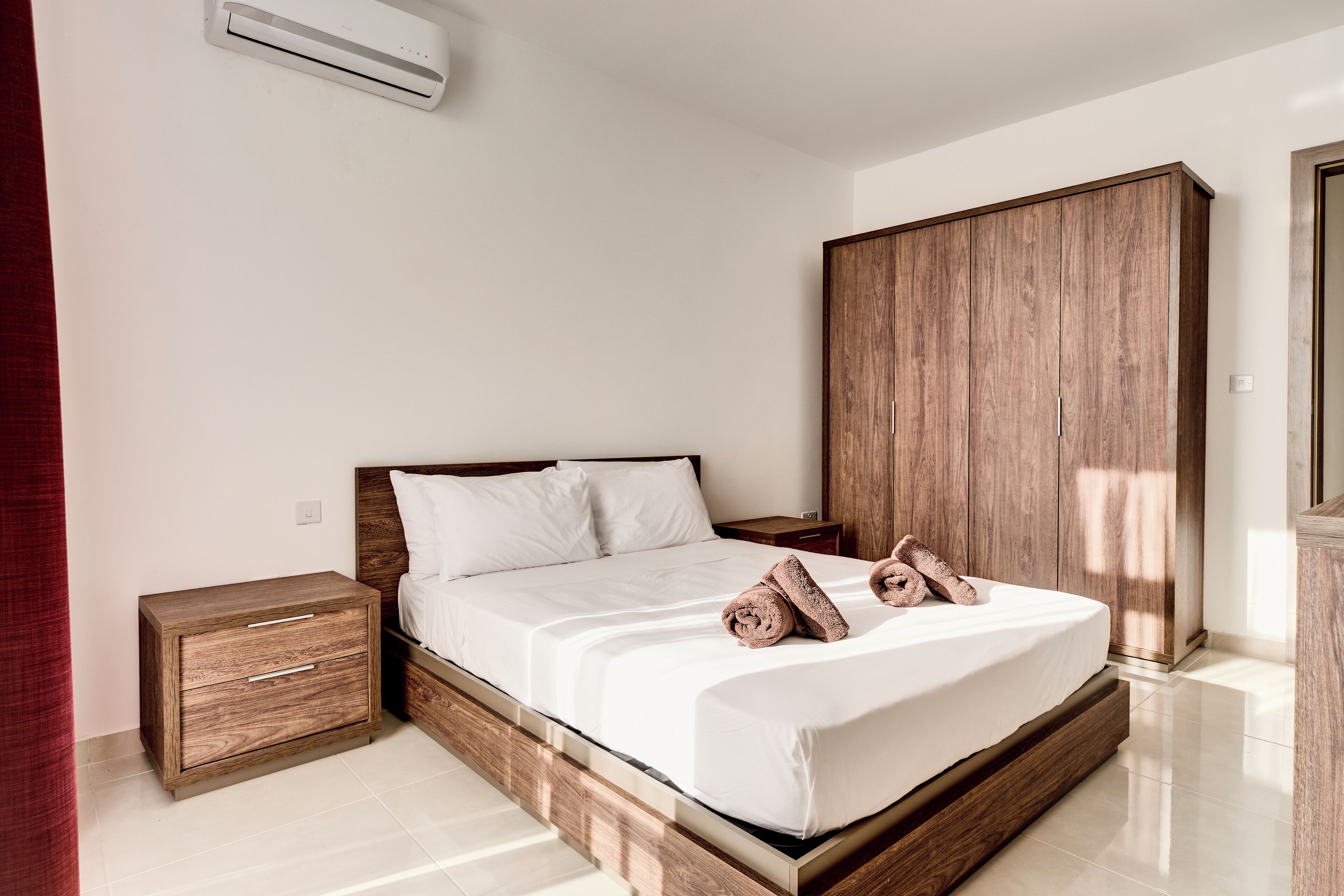 Ein Schlafzimmer mit hölzernem Bettgestell, weißer Bettwäsche, einem Nachttisch und einem Kleiderschrank.