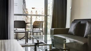 A modern living room with a glass coffee table, two chairs, a sofa, and a large window offering a city view. - The Village Apartments (St. Paul's Bay)