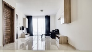 A modern living room with a flat-screen TV, a sofa, and a coffee table. - The Village Apartments (St. Paul's Bay)