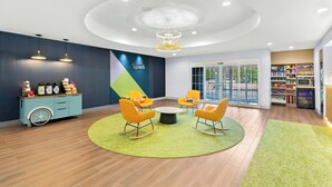 A modern interior with a blue wall, a green rug, yellow chairs, a round table, and a ceiling light. - Spark by Hilton Missouri City (Missouri City)