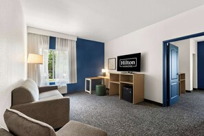 A hotel room with a sofa, a TV, a desk, and a minibar. - Spark by Hilton Missouri City (Missouri City)