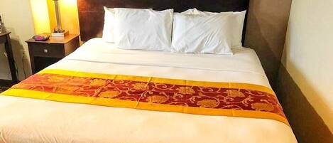 A hotel room with a bed, a nightstand, a lamp, and a patterned bedspread.