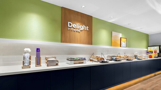 A buffet counter with a sign reading 'Delight in the day,' a variety of food items, and a clean, modern design. - Spark by Hilton Missouri City (Missouri City)