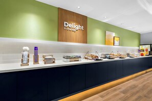 A buffet counter with a sign reading 'Delight in the day,' a variety of food items, and a clean, modern design. - Spark by Hilton Missouri City (Missouri City)